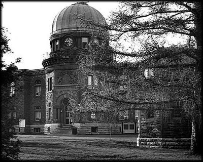 Photo en noir et blanc d'un bâtiment en pierre avec un toit en dôme, partiellement caché par un arbre.