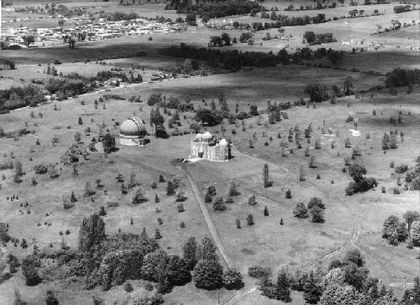 Photo aérienne en noir et blanc deux bâtiments à dôme, avec quelques jeunes arbres autour et une concentration de résidences en haut à gauche