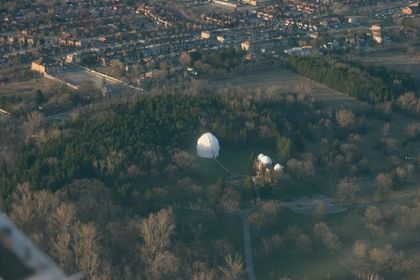 Aerial photo of two buildings with white domes, surrounded by a woodlot and bordered by a large residential neighbourhood
