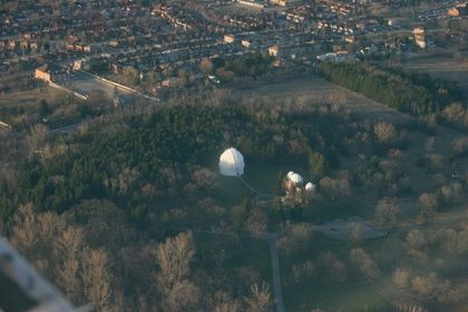 Photo aérienne de deux bâtiments à dôme blanc, entourés d'un boisé et bordé par un large ensemble résidentiel