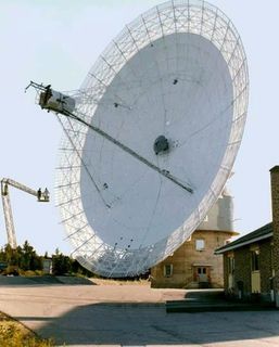 Close-up photo of a white antenna attached to a circular building to the right of a lift with two people aboard