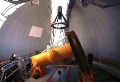 Photo of the structure of a yellow and white telescope pointing towards the sky through an opening in a white dome