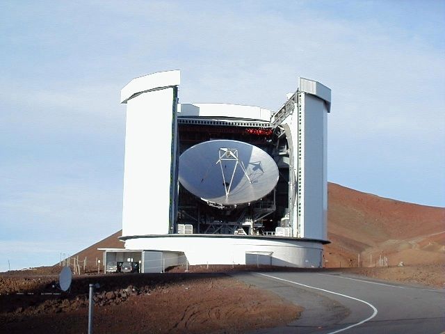 Photo of the exterior of a circular white building open along its facade. Inside, a white telescope points towards the sky