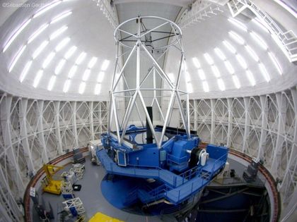 Photo de l'intérieur d'un observatoire avec un dôme fermé. Les murs sont blancs et la base du télescope est bleue.