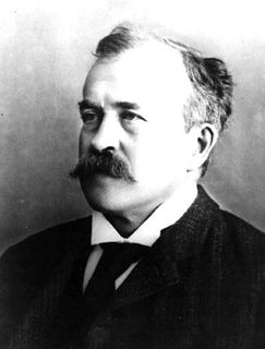 Black and white photo of a man with a long mustache wearing a black jacket and looking to his right