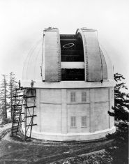 Photo en noir et blanc d'un bâtiment cylindrique blanc, avec un toit en dôme ouvert, un escalier sur le côté gauche mène au rebord du dôme