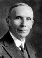 Black and white photo of a man in profile looking at the lens and wearing a suit and tie