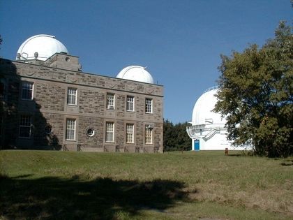 Photo of a stone building and three white domes, one of which is partially hidden by a tree