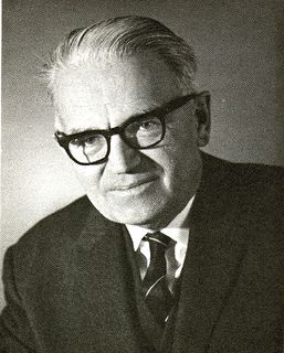 Black and white photo of a man with black-rimmed glasses wearing a suit and tie