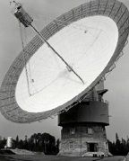 Antenne au coeur blanc et au pourtour en structure métallique, pointant vers le ciel et supportée par un bâtiment cylindrique