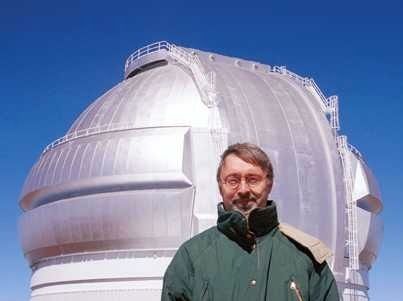 Photo d'un homme portant un manteau vert et des lunettes devant un bâtiment à dôme métallique de couleur argentée