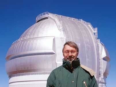 Photo of a man with glasses wearing a green coat in front of a  building with a silver-coloured metal dome