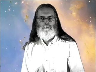 Black and white photo of a man with a beard and long hair wearing glasses against a starry blue and yellow background