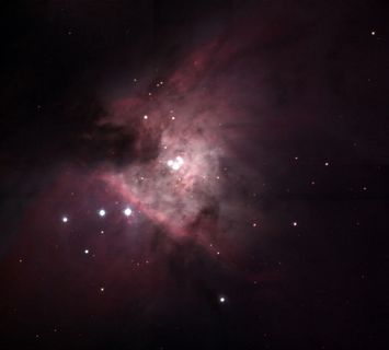 Photo d'une nébuleuse, constituée des points blancs très lumineux et de nuages aux nuances rosées sur un fond très noir