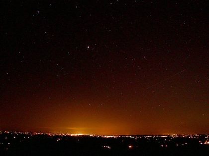 Photo of an orange glow on the horizon of a black starry sky, above urban lighting