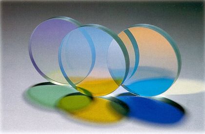 Trois pastilles transparentes, mauves, bleues et orange, contenant des filtres UV et juxtaposées à la verticale, traversées de lumières créant des ombres vertes, jaunes et bleues.
