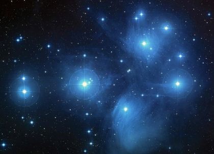 Photograph of a group of dots of white light surrounded by vaporous blue halos in a black sky