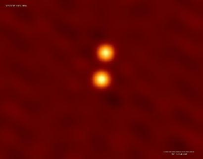 Deux points orange superposés et entourés d'un halo jaunâtre sur fond rouge.