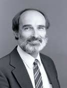 Black and white photo of a bearded man smiling and wearing a suit.