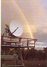 Photo couleur d'une antenne blanche installée sur une structure métallique devant un arc-en-ciel