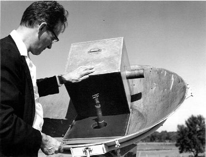 Photo en noir et blanc d'un homme de profil, portant des lunettes et observant le mécanisme d'une antenne.