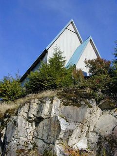 Photo of two conical white roofs at the top of a rocky hill, hidden by small coniferous trees