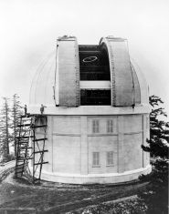 Black and white photo of a cylindrical white building with a white dome that is open and a stairway on the left leading to the side of the dome
