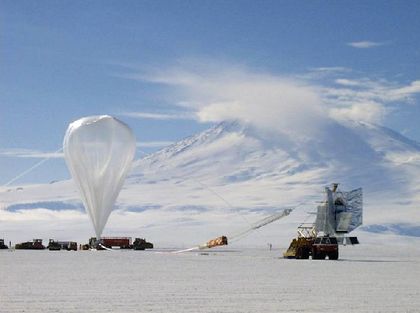 Photo of a balloon attached to a telescope installed on the platform of a truck in the desert, with a high, snow-covered mountain in the background