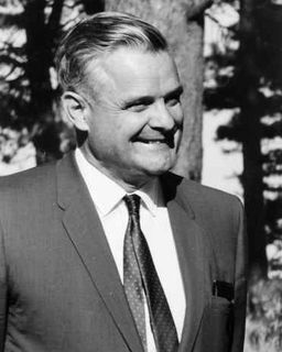 Photo en noir et blanc d'un homme souriant, regardant vers sa gauche et portant un complet