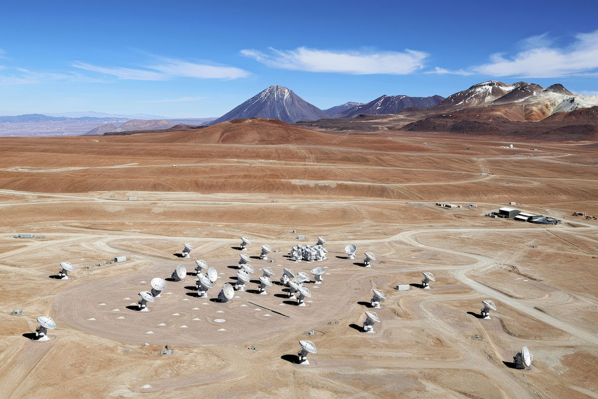 Photo of a group of white antennas aimed towards the sky and located in the desert with mountains and a blue sky on the horizon